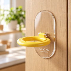 The yellow ring and clear base toilet seat lifter are shown attached to a light wooden surface.