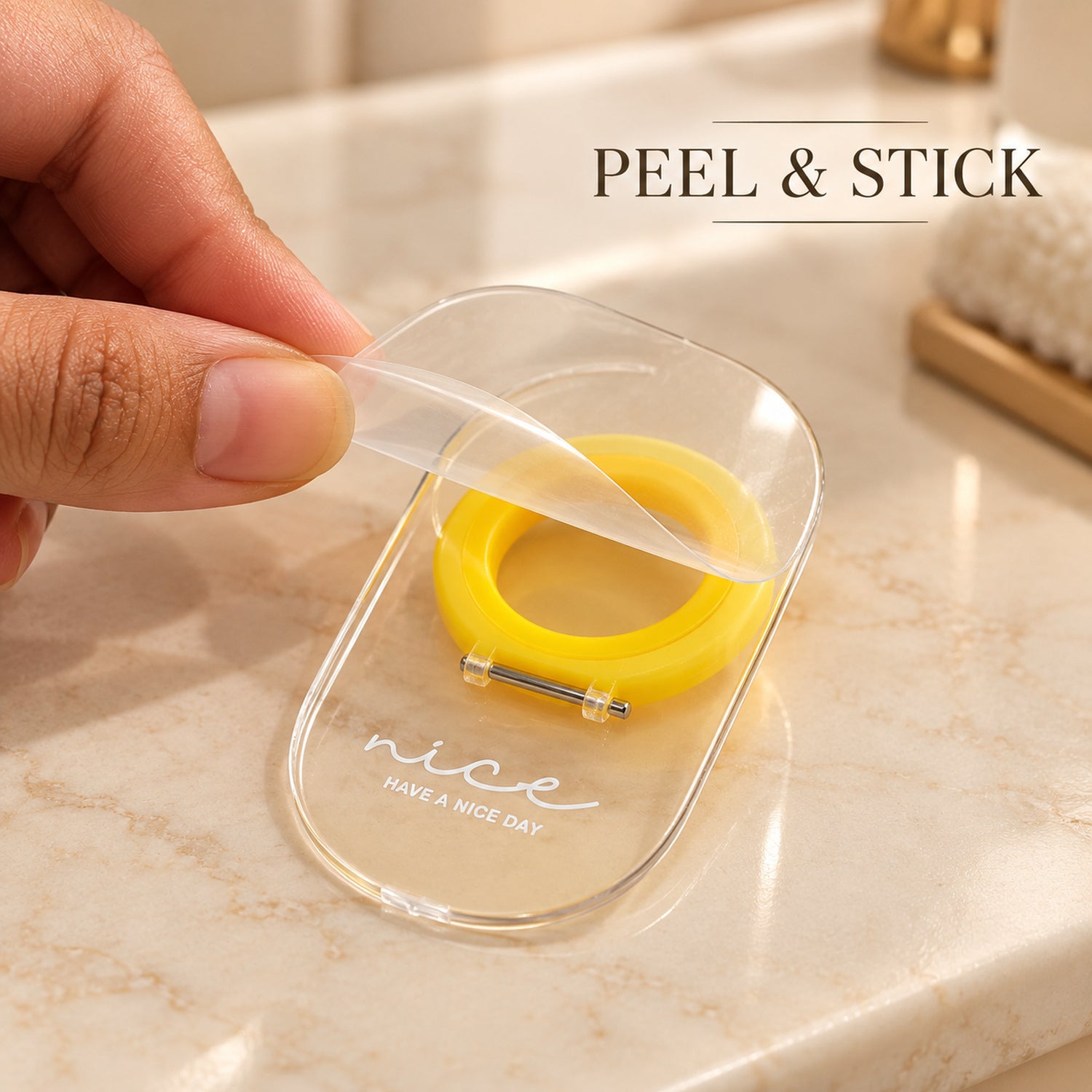 A hand peels the protective film from the clear adhesive base of the toilet seat lifter.