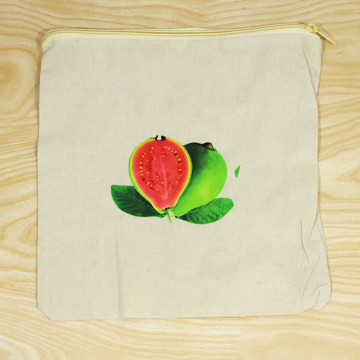 Empty cream cotton storage bag with a guava print and a yellow zipper, laid flat on wood.