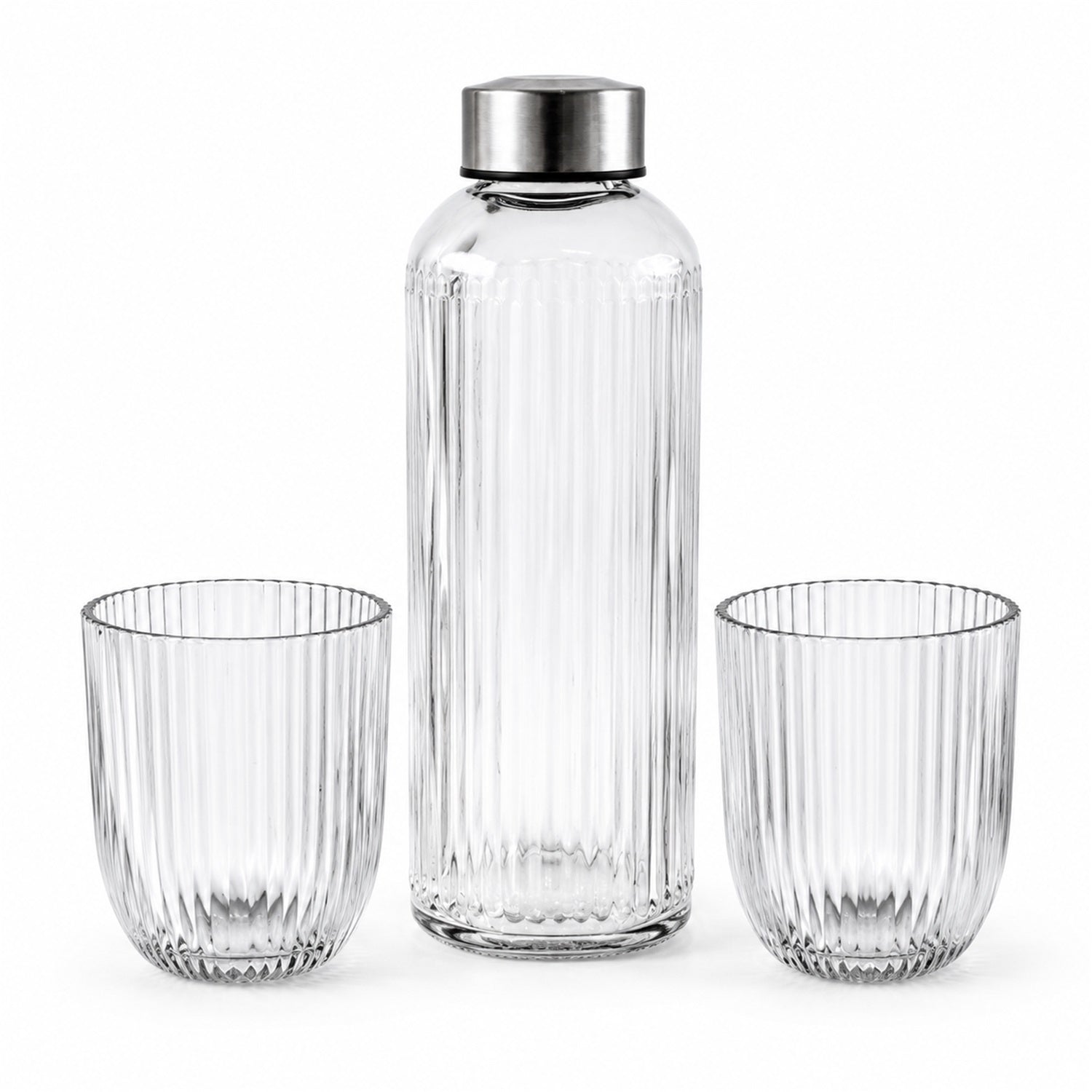 A clear ribbed glass bottle with a silver cap stands between two empty matching ribbed glass tumblers on a plain white