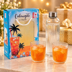A blue gift box with a tropical design sits beside a clear ribbed glass bottle and two matching tumblers filled with orange