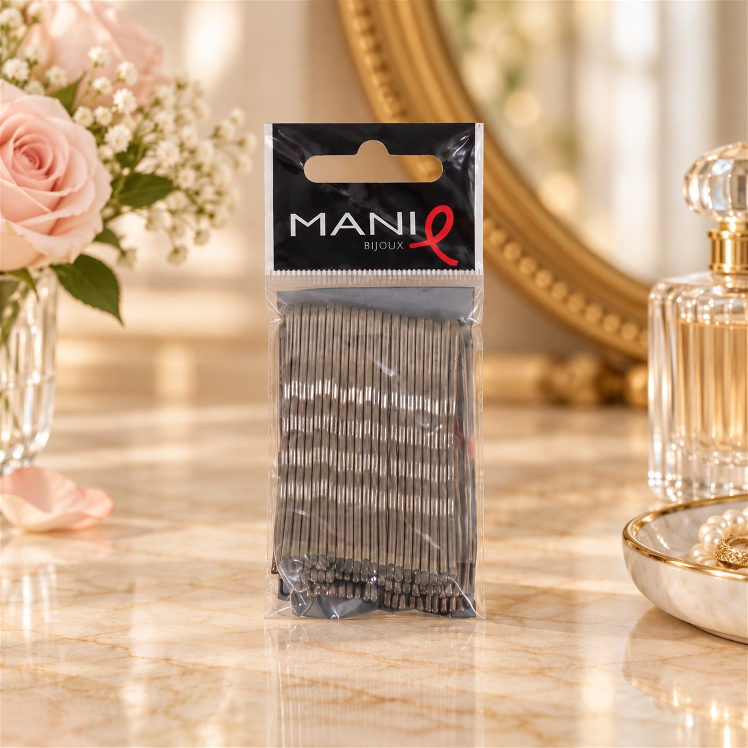 A clear plastic package of grey metal bobby pins sits on a marble vanity, surrounded by perfume bottles and flowers.