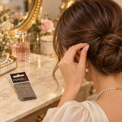 A woman with brown hair inserts a grey metal bobby pin into her elegant bun, sitting at a vanity table.