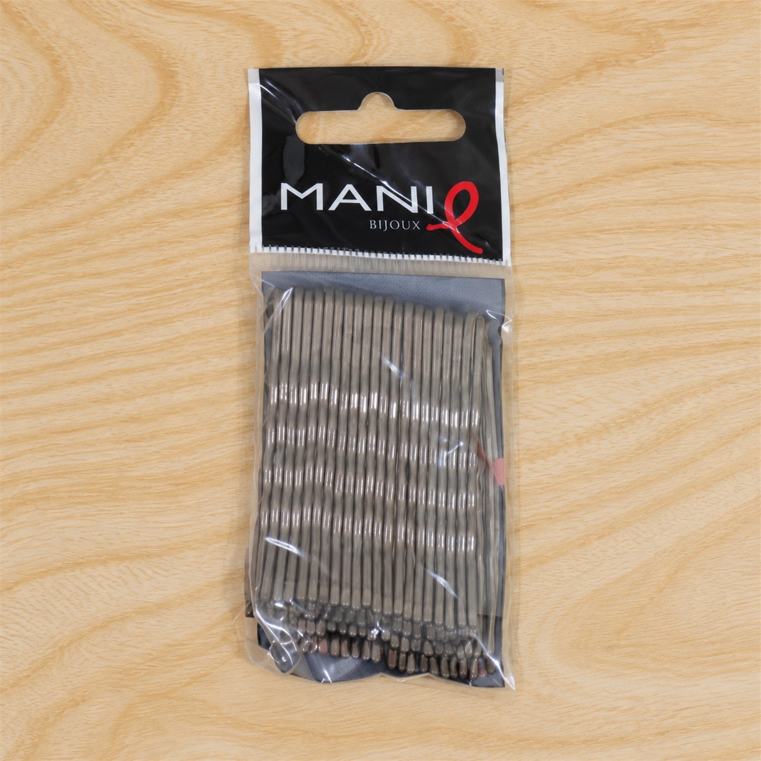 A clear plastic package of grey metal bobby pins is centered on a light wooden surface.