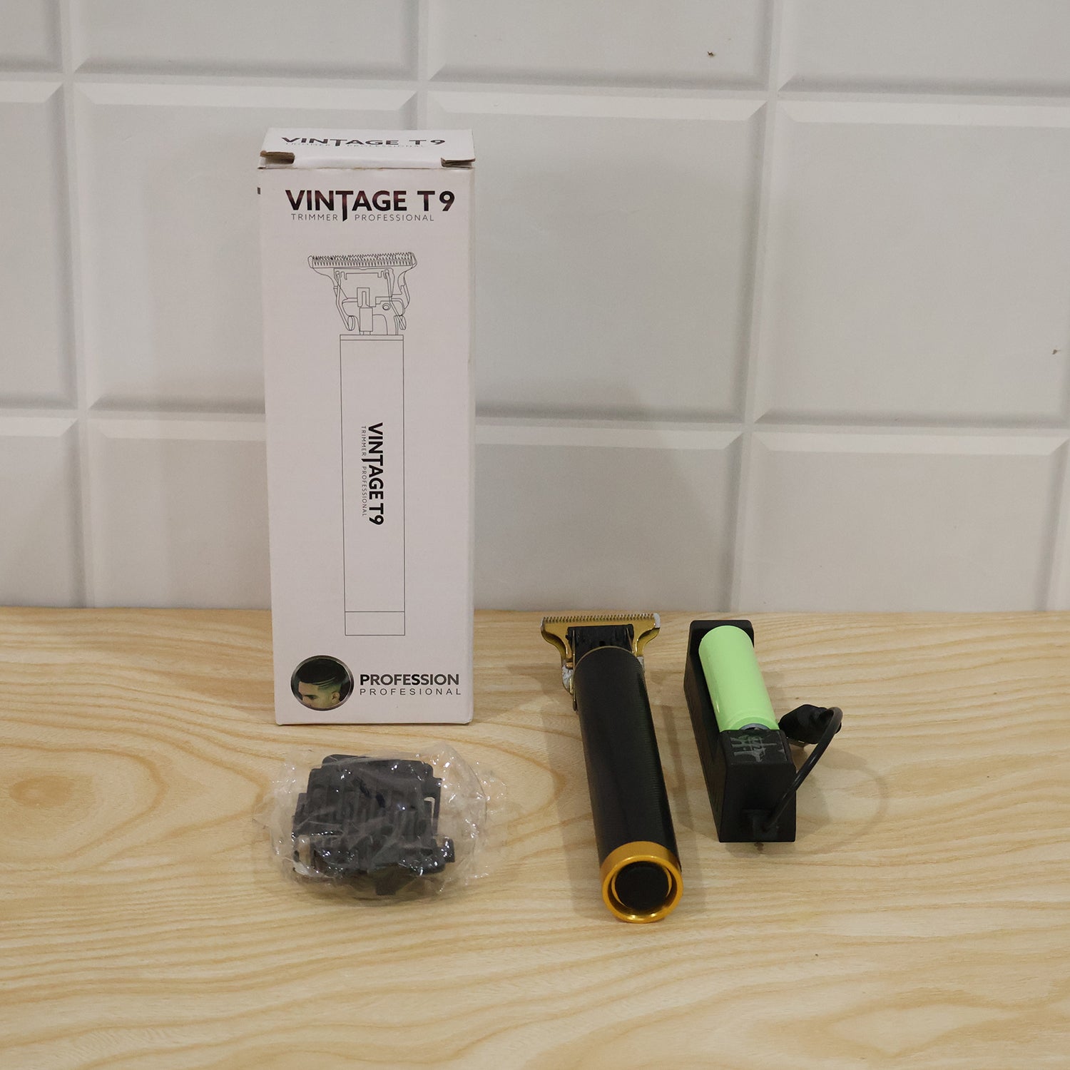 A white box labeled 'VINTAGE T9' stands next to the black and gold trimmer, a clear bag of combs, and a battery charger on a