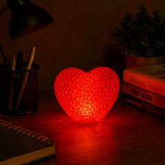 A red heart-shaped crystal texture LED lamp glowing brightly on a dark wooden desk next to office supplies.