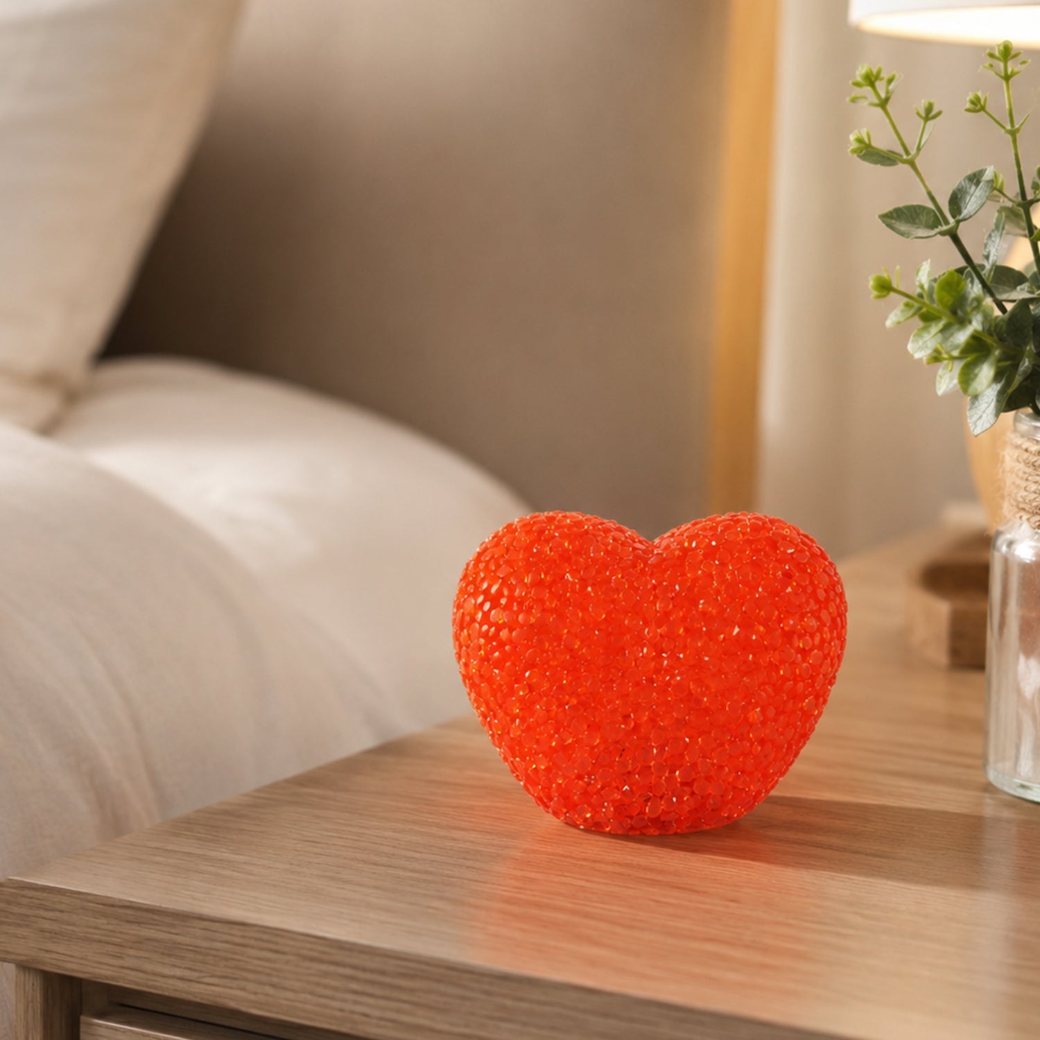 A red heart-shaped LED night lamp rests on a wooden nightstand beside a small plant in a clear vase.