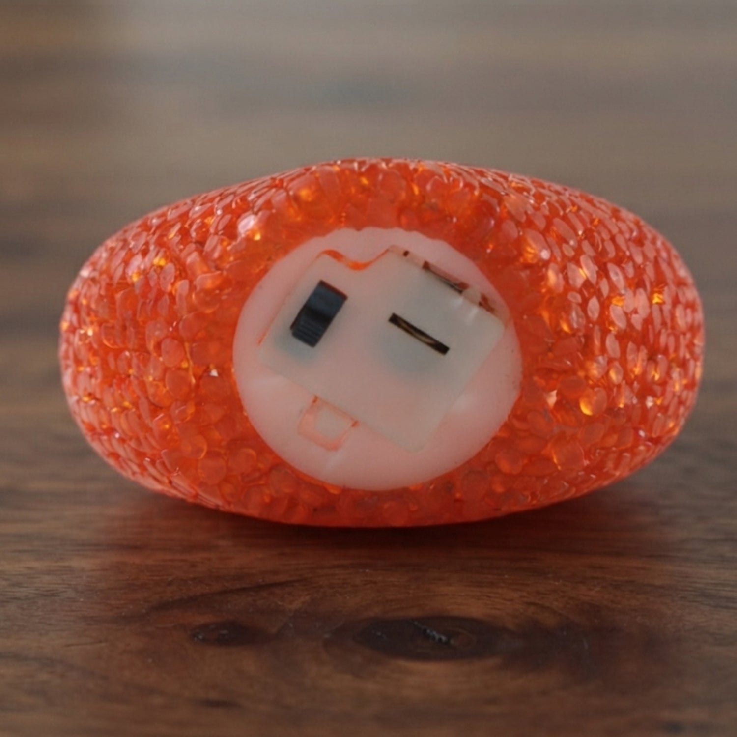 The underside of an orange heart-shaped LED lamp reveals its battery compartment on a wooden surface.