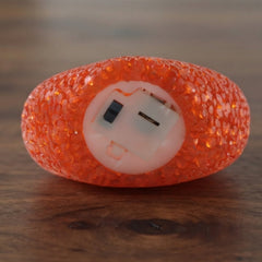 The underside of an orange heart-shaped LED lamp reveals its battery compartment on a wooden surface.