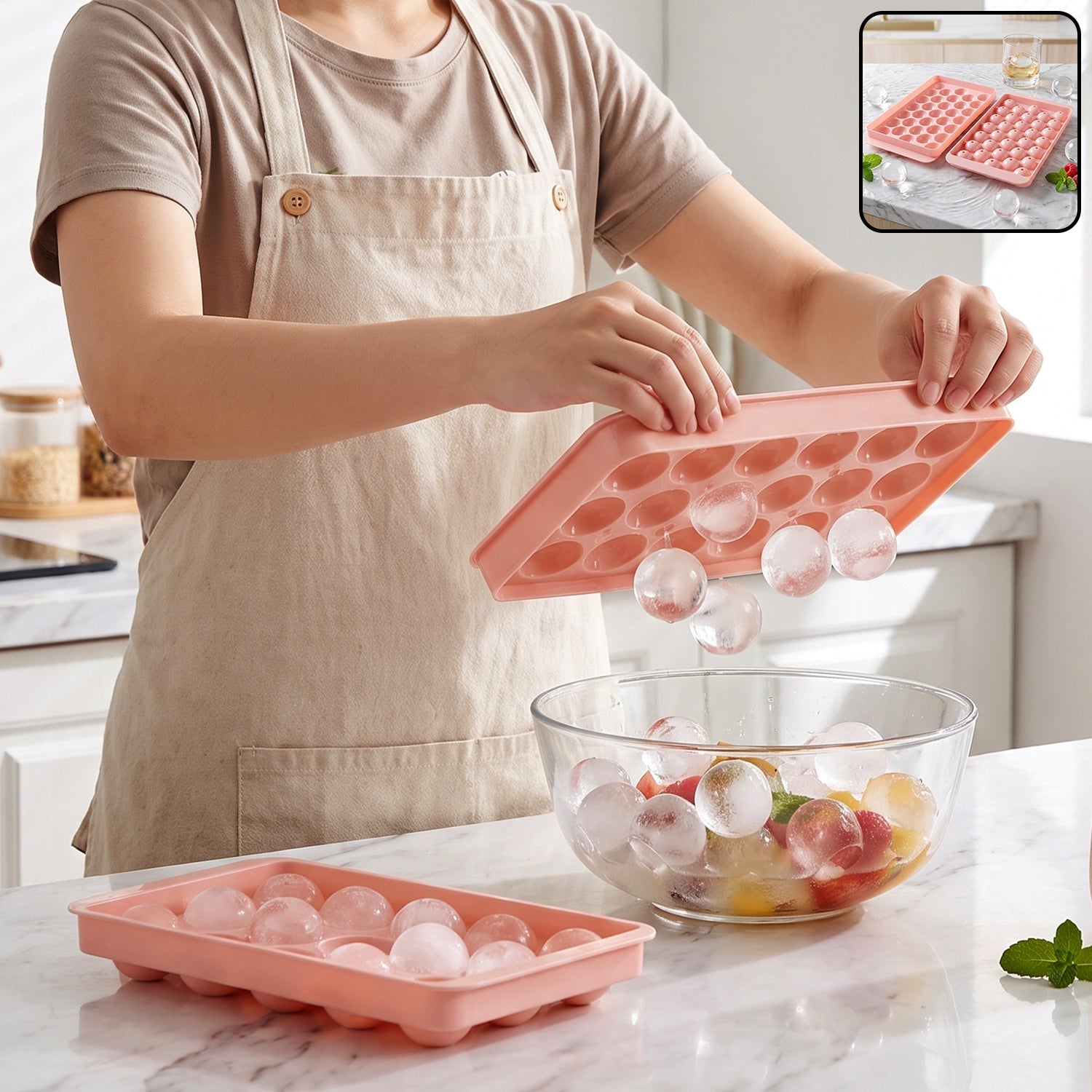 A person in an apron holds a pink ice ball tray, releasing clear ice balls into a glass bowl of fruit.