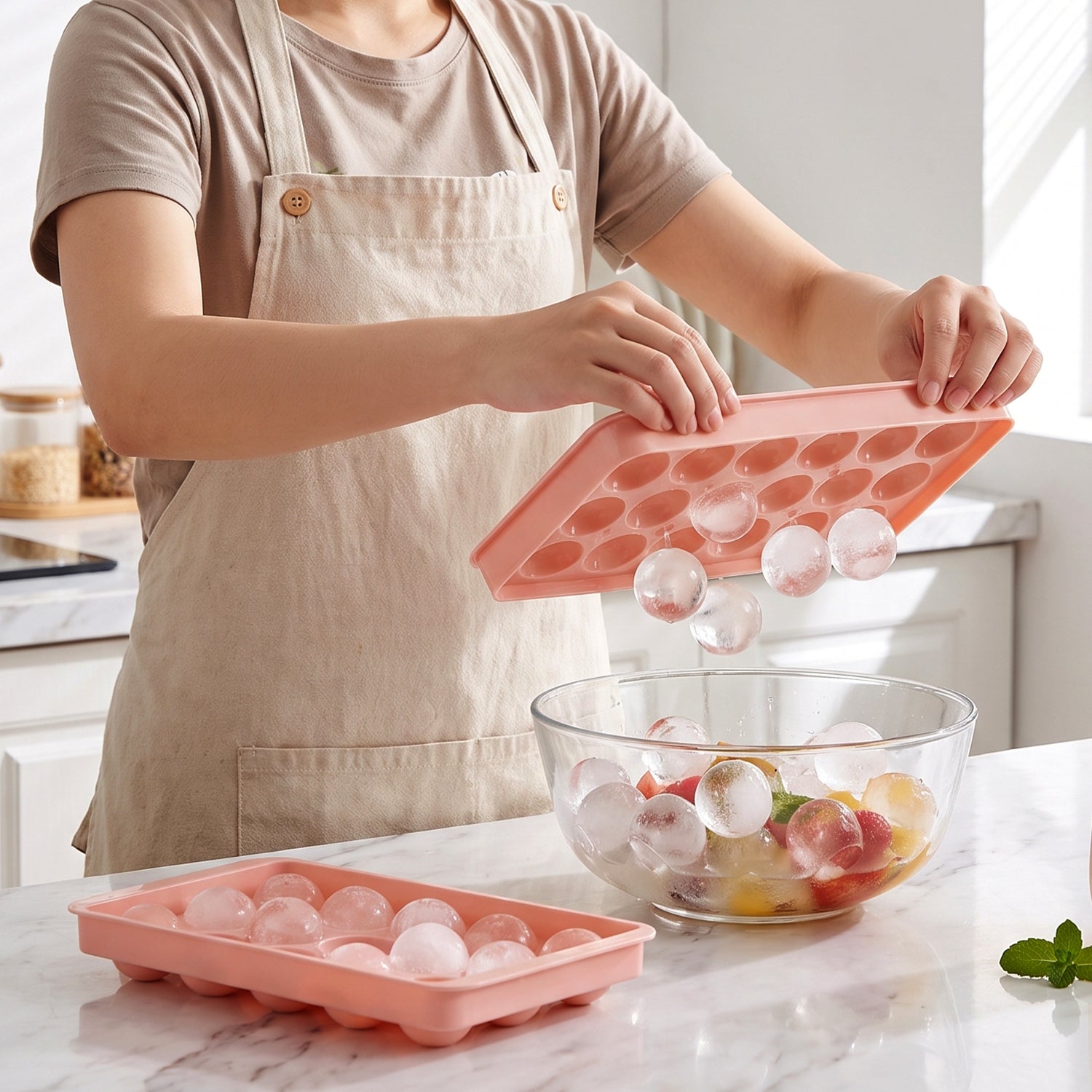 Person using a pink ice ball tray to add clear ice balls to a fruit-filled glass bowl.