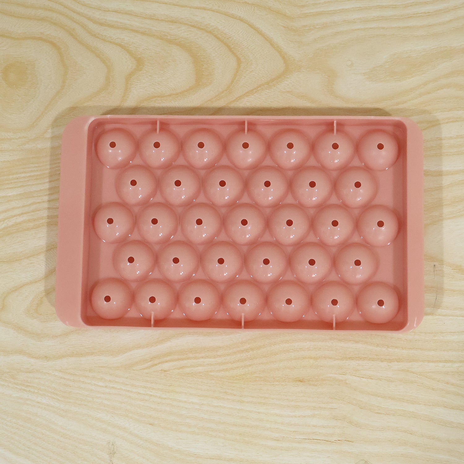 A single pink plastic ice ball tray with 33 spherical molds on a light wooden surface.