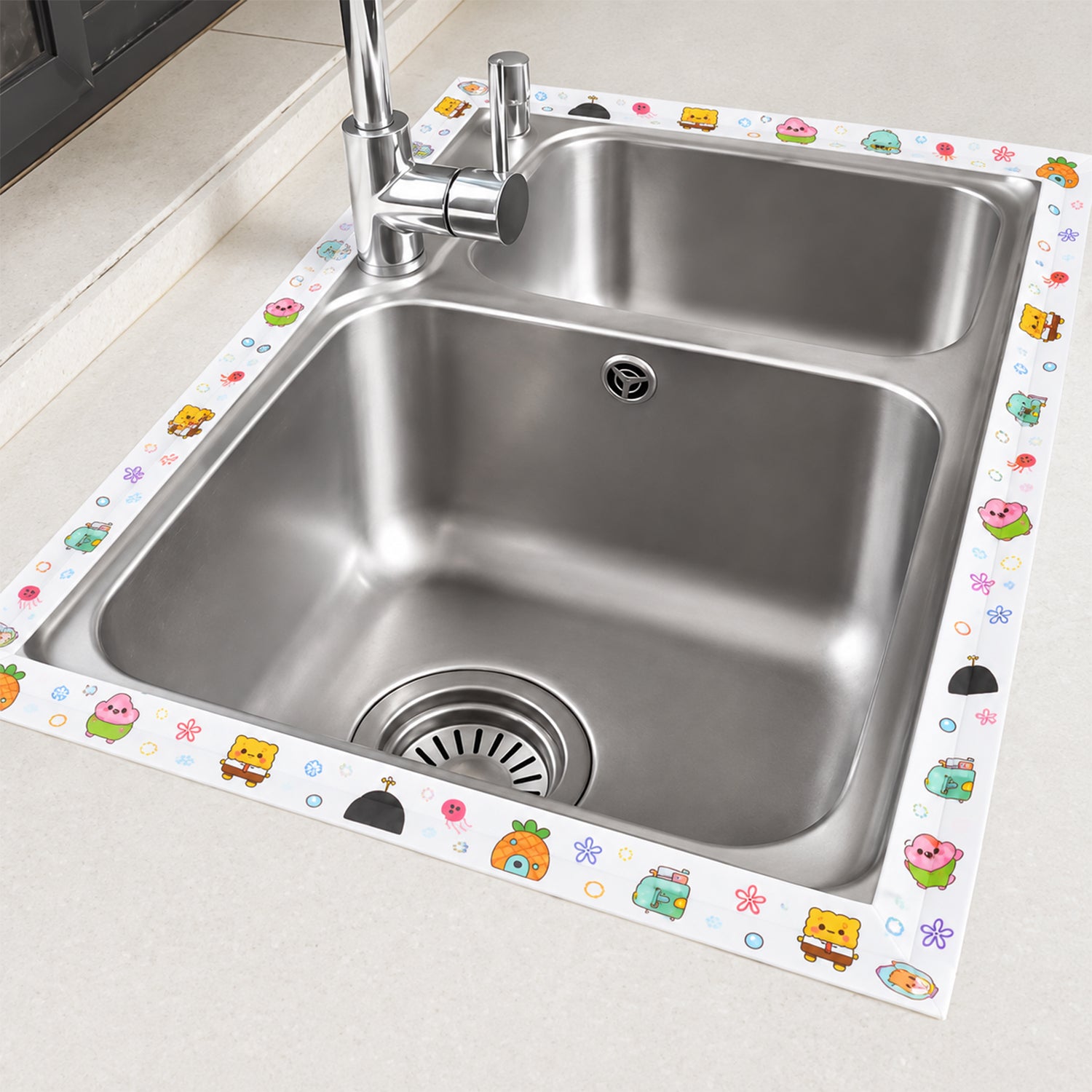 The cartoon-printed sealing tape is applied around the perimeter of a double stainless steel kitchen sink.