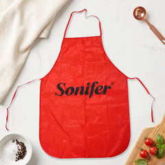 A flat lay of a red Sonifer apron on a white marble surface with spices, tomatoes, and a measuring spoon.