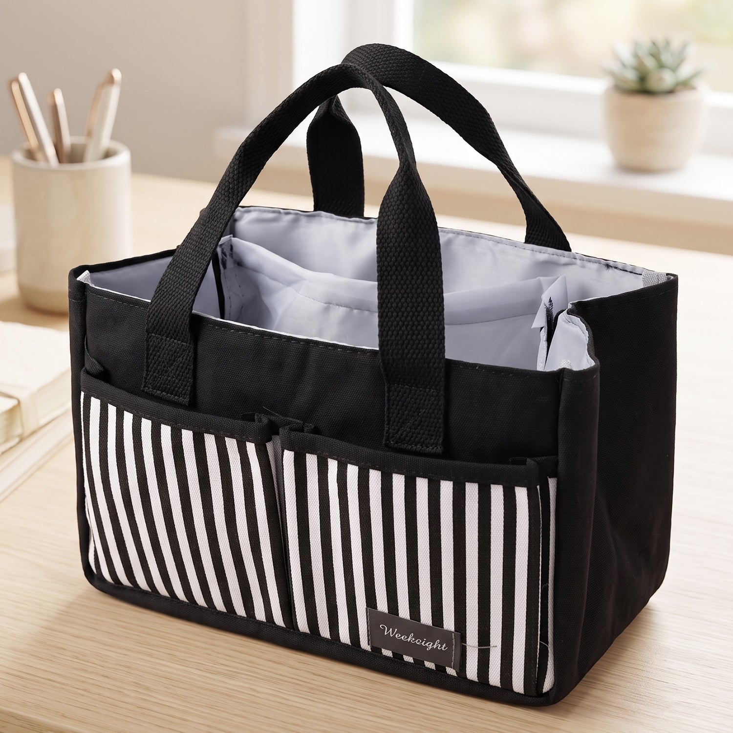 An empty black and white striped organizer bag caddy with handles sits on a wooden desk, ready for use.