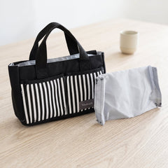 A black and white striped organizer bag caddy with handles sits next to a folded gray fabric divider on a wooden table.