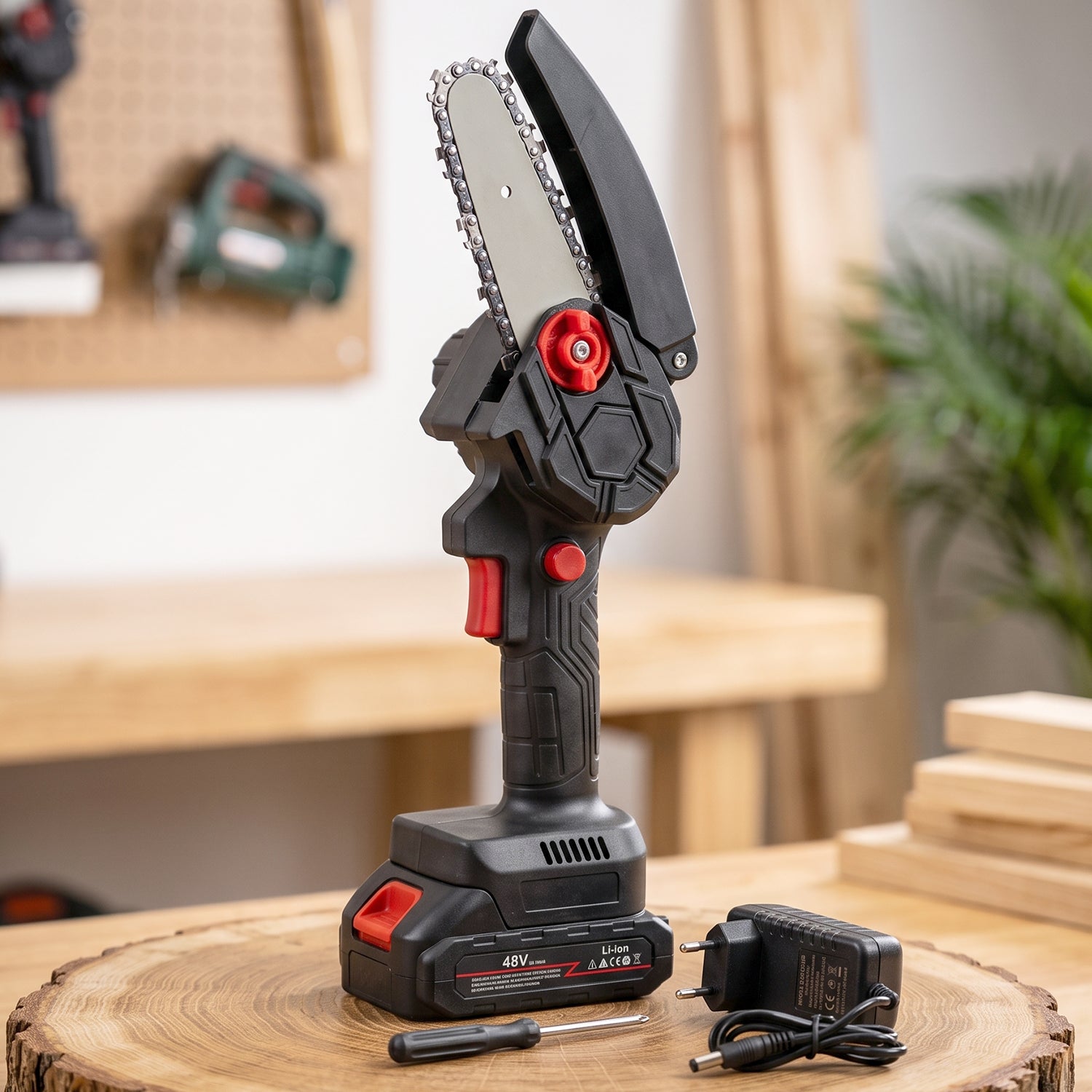 Gloved hand holding a black and red mini chainsaw, cutting a tree branch in a sunny garden.