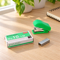 A vibrant green mini stapler rests beside a box of No. 10 staples and loose metal staples on a wooden desk.
