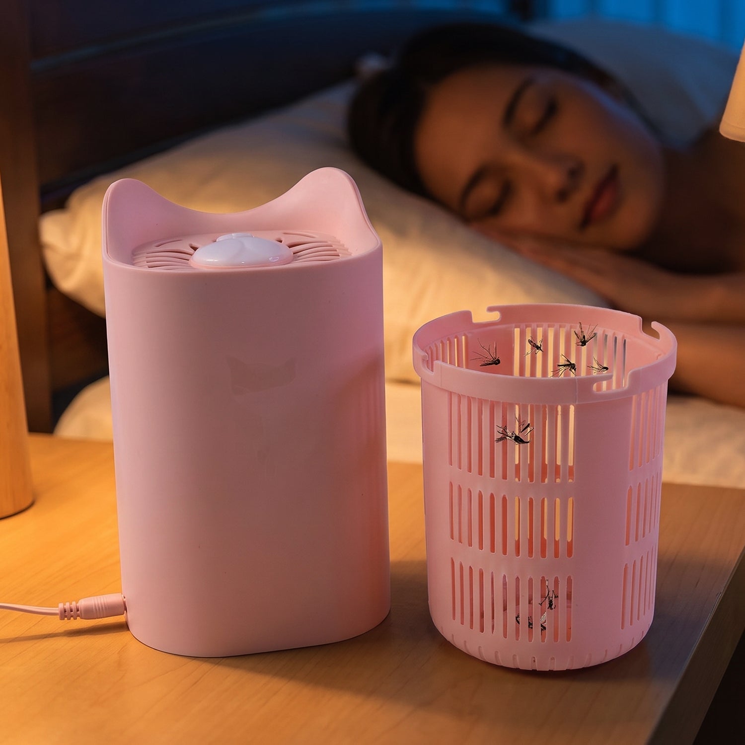 A pink cat-shaped mosquito killer lamp and its collection basket, containing several dead mosquitoes, are on a nightstand