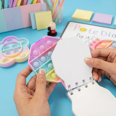 A person's hands opening a pastel hexagon pop it fidget notebook, revealing the colorful pop it cover.