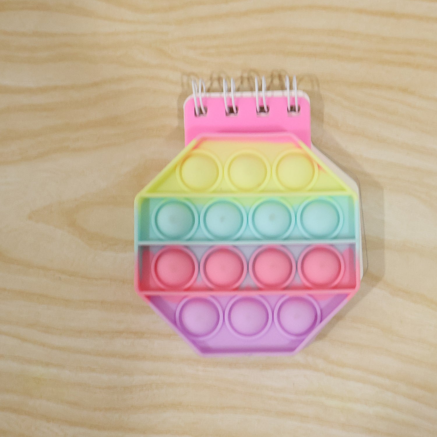 A pastel hexagon pop it fidget notebook with a pink spiral binding on a light wooden surface.