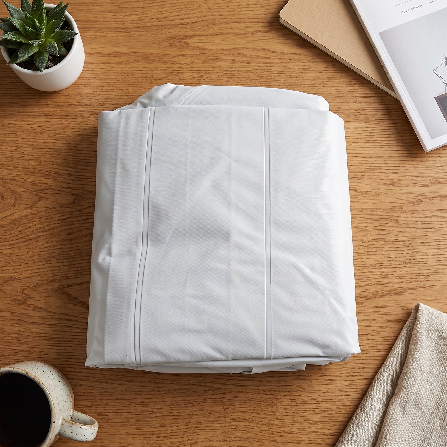 A neatly folded white inflatable mat is placed on a wooden table next to a small potted plant and a mug.