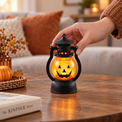 A hand gently touches a glowing pumpkin lantern on a wooden coffee table, surrounded by autumn decor.