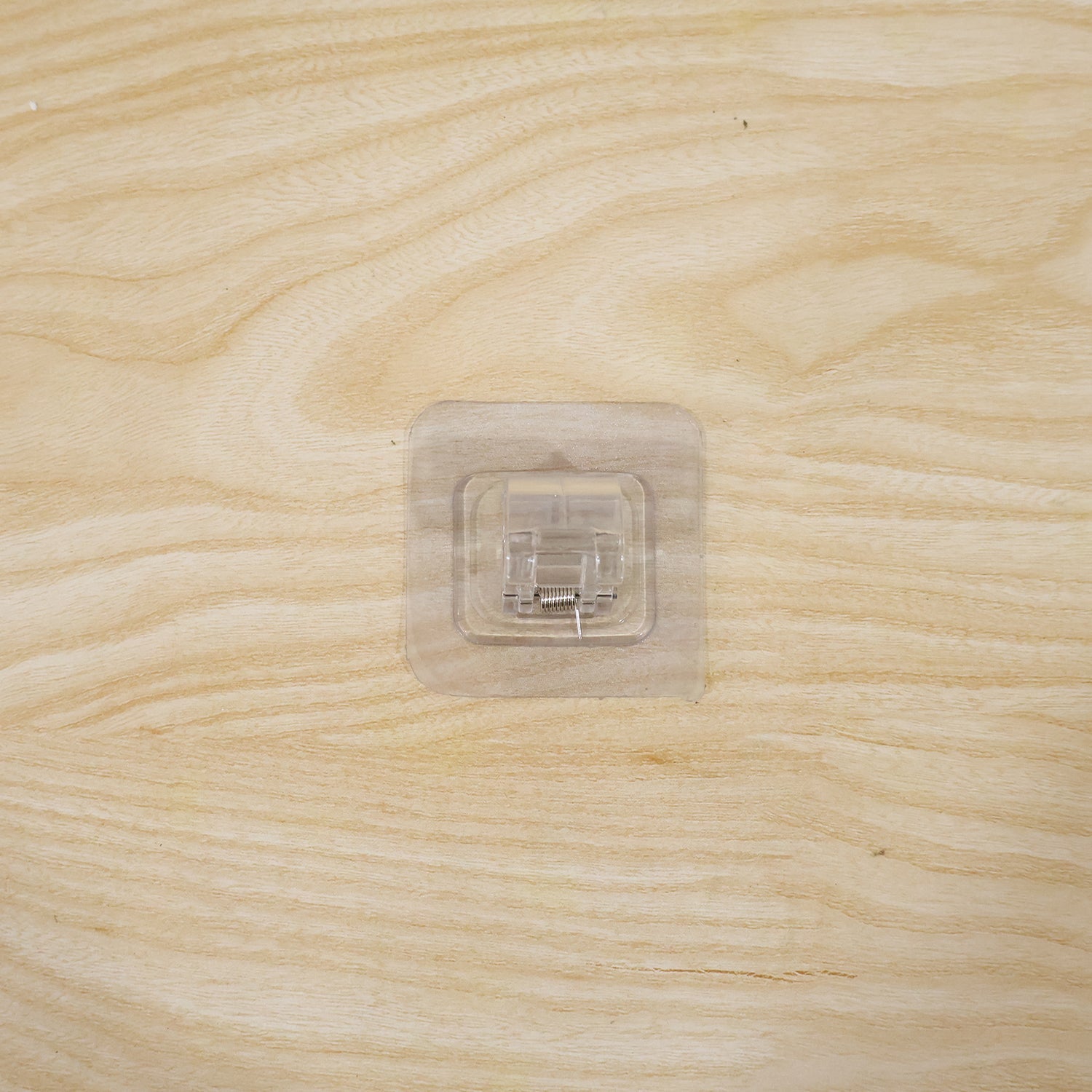 Transparent self-adhesive wall hook in use mounted on wall