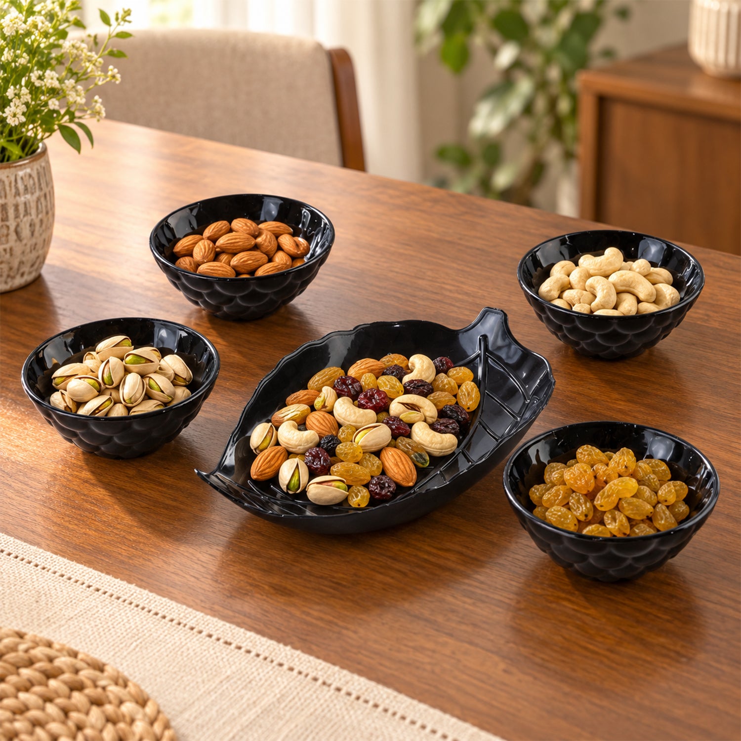 A black leaf-shaped platter holds mixed nuts, surrounded by four small black bowls filled with various dry fruits.