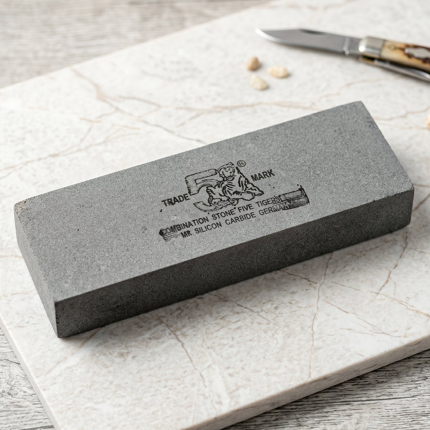 A gray silicon carbide whetstone with a tiger logo and text rests on a white marble surface.