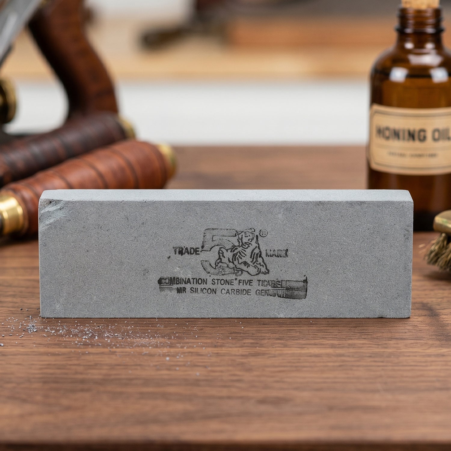 A gray silicon carbide whetstone sits on a wooden surface with a bottle of honing oil in the background.
