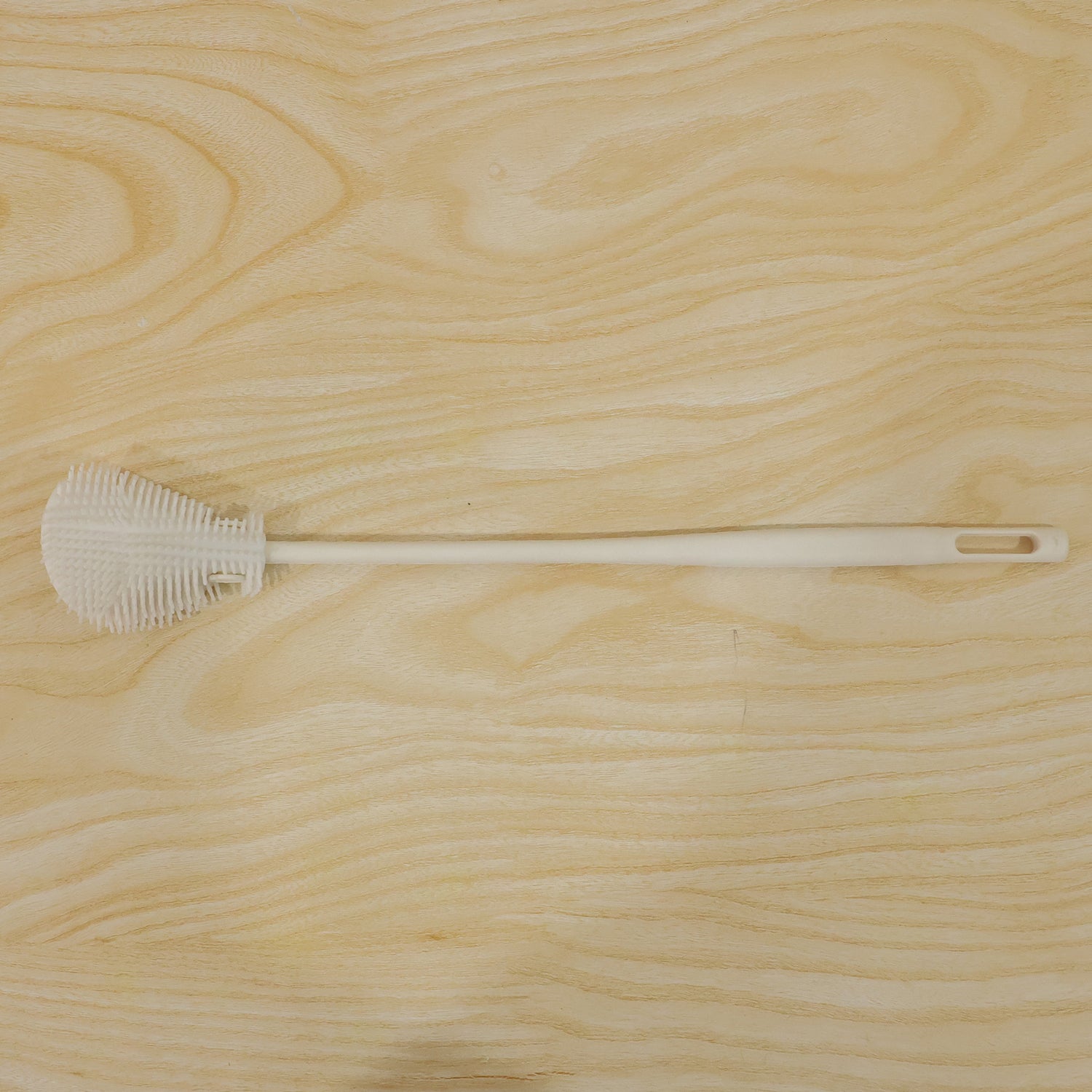 A white silicone bottle cleaning brush with a textured head and a hanging hole, laid flat on a light wooden surface.