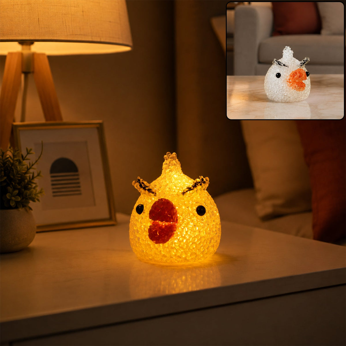 A glowing yellow chick-shaped night lamp with crystal texture sits on a white nightstand beside a lamp and framed picture.