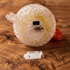 The underside of the chick-shaped lamp reveals the battery compartment and a white plastic cover on a wooden surface.