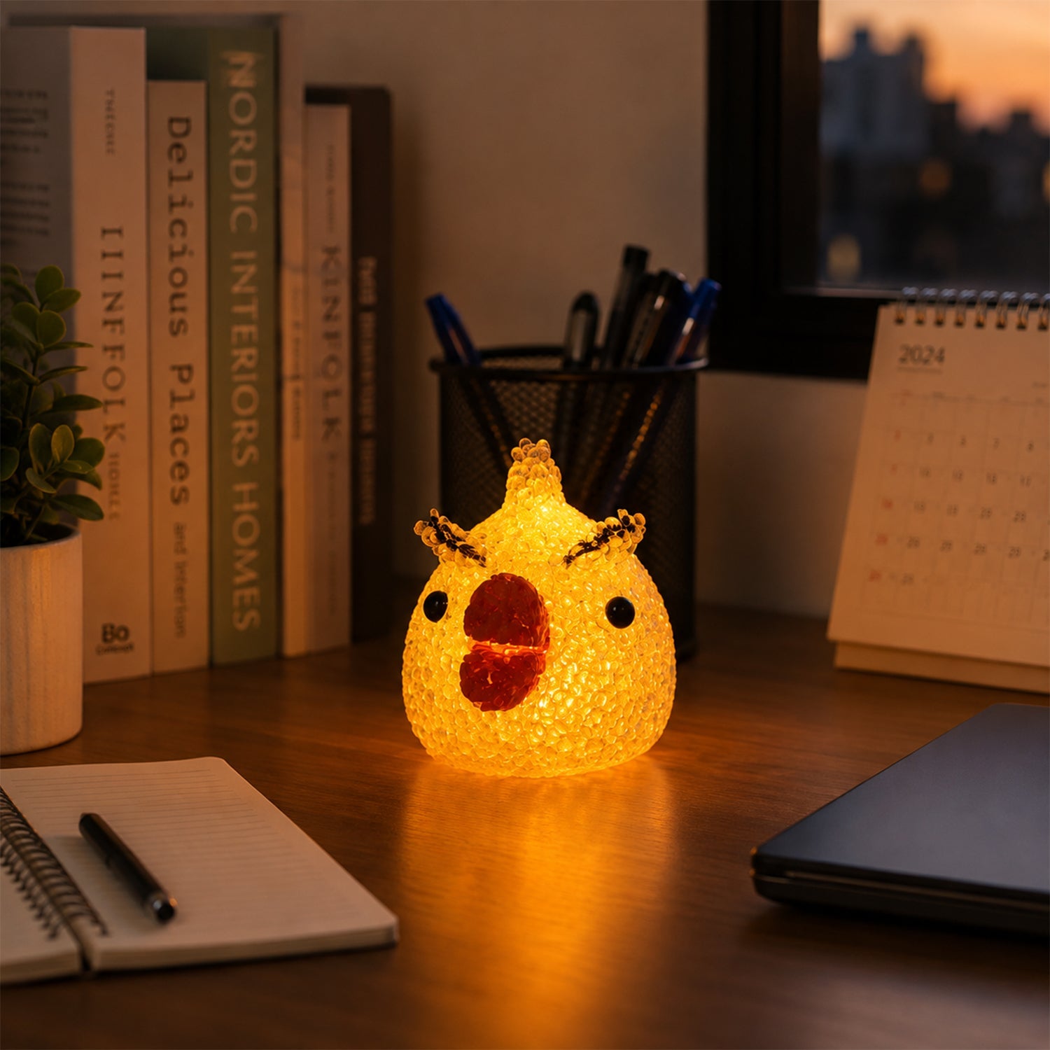 A glowing yellow chick-shaped night lamp on a wooden desk with books, a pen holder, and a calendar in the background.