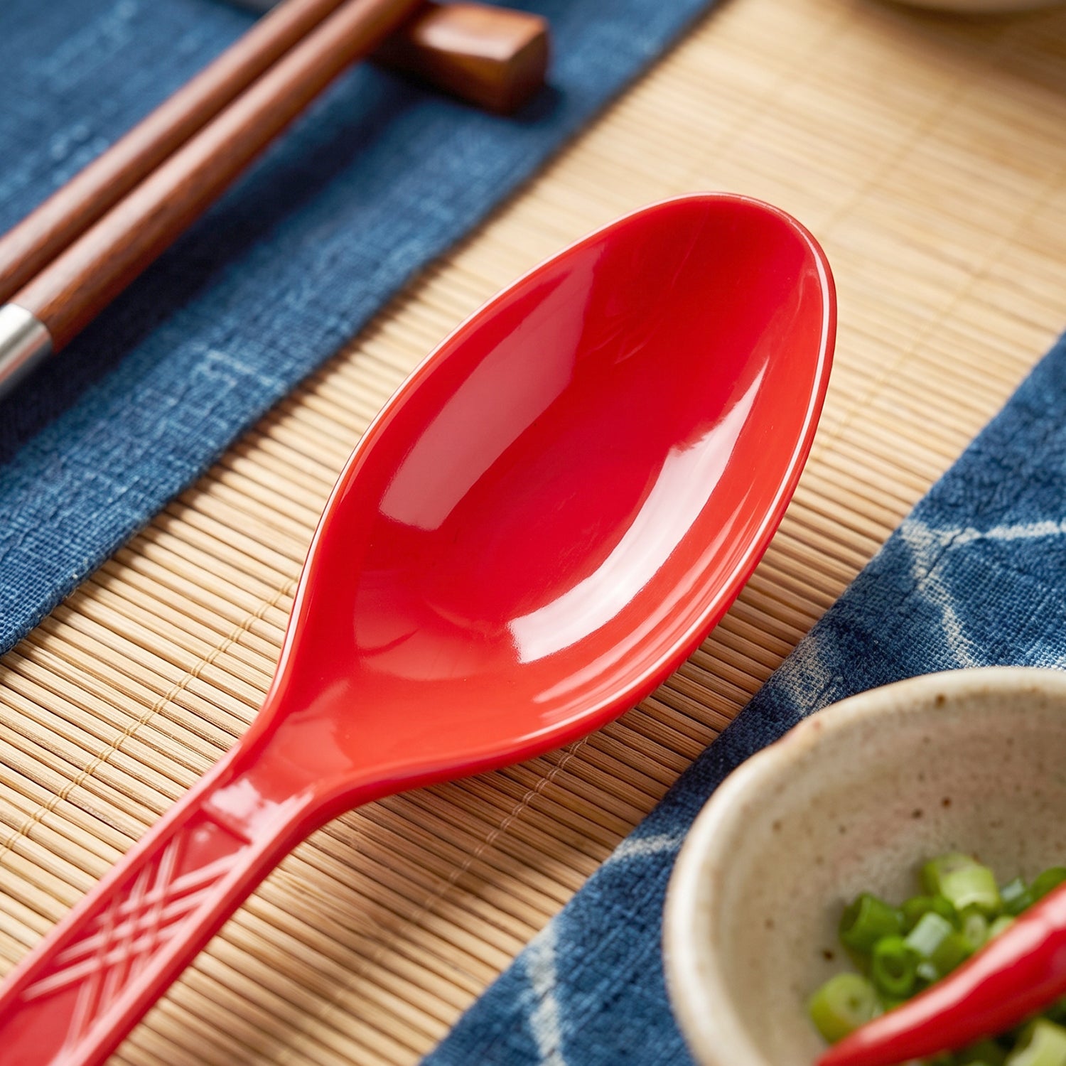 Close-up of a single red plastic spoon with a textured handle on a blue and bamboo mat.