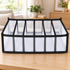 A white mesh and black fabric 6-section drawer organizer sits on a light wooden table in a bright room.