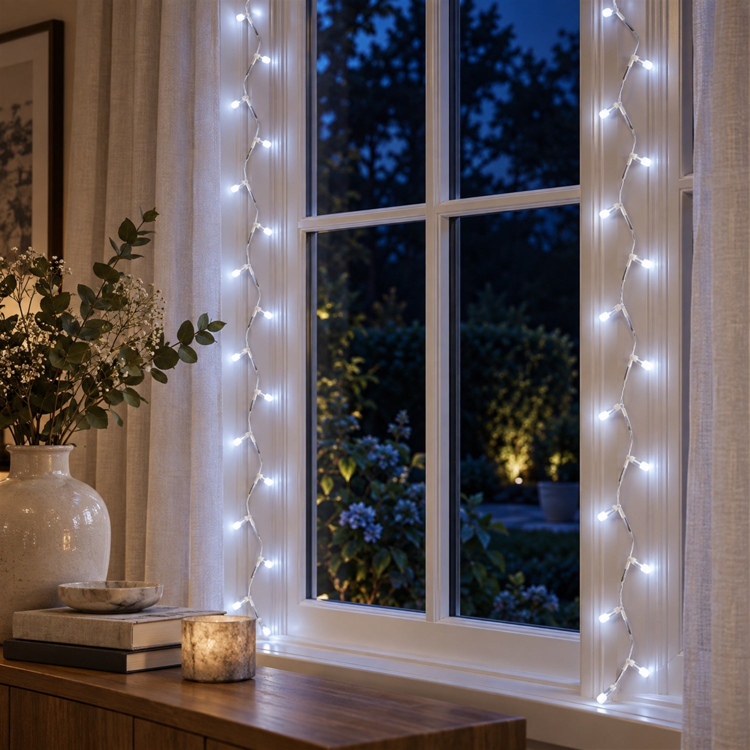 White LED string lights hanging vertically on a window frame, illuminating a dark garden outside.