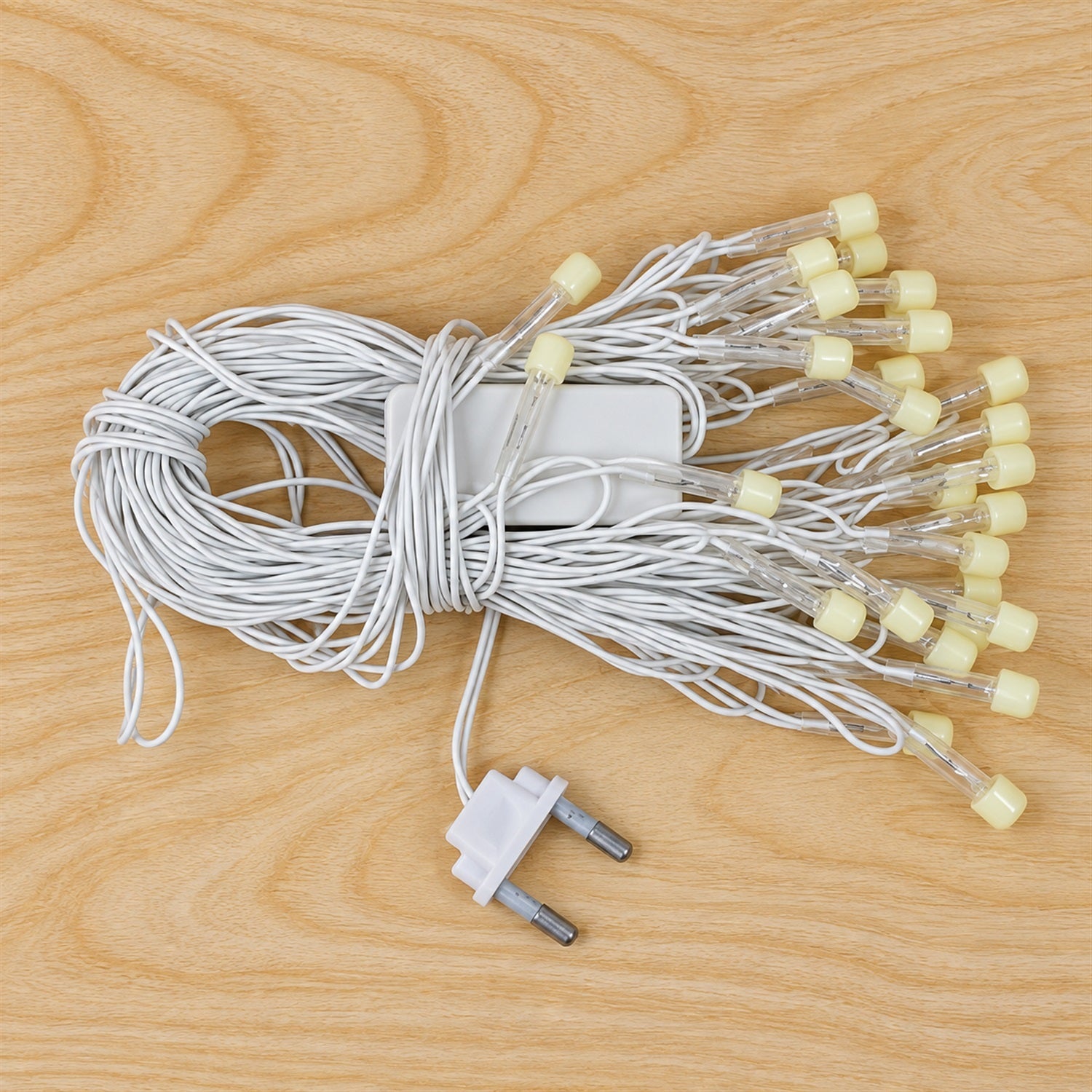 A coiled white string of LED lights with a two-pin electrical plug on a light wooden surface.