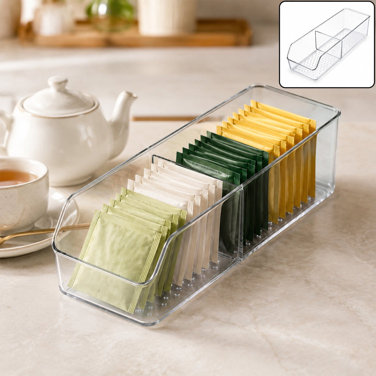 Clear plastic organizer with two compartments filled with various colored tea bags on a kitchen counter next to a teapot and