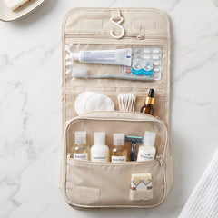 An open beige toiletry bag hanging, displaying multiple compartments with various personal care items.