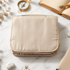 A folded beige toiletry bag on a marble surface with a compass, open book, and small white stones.