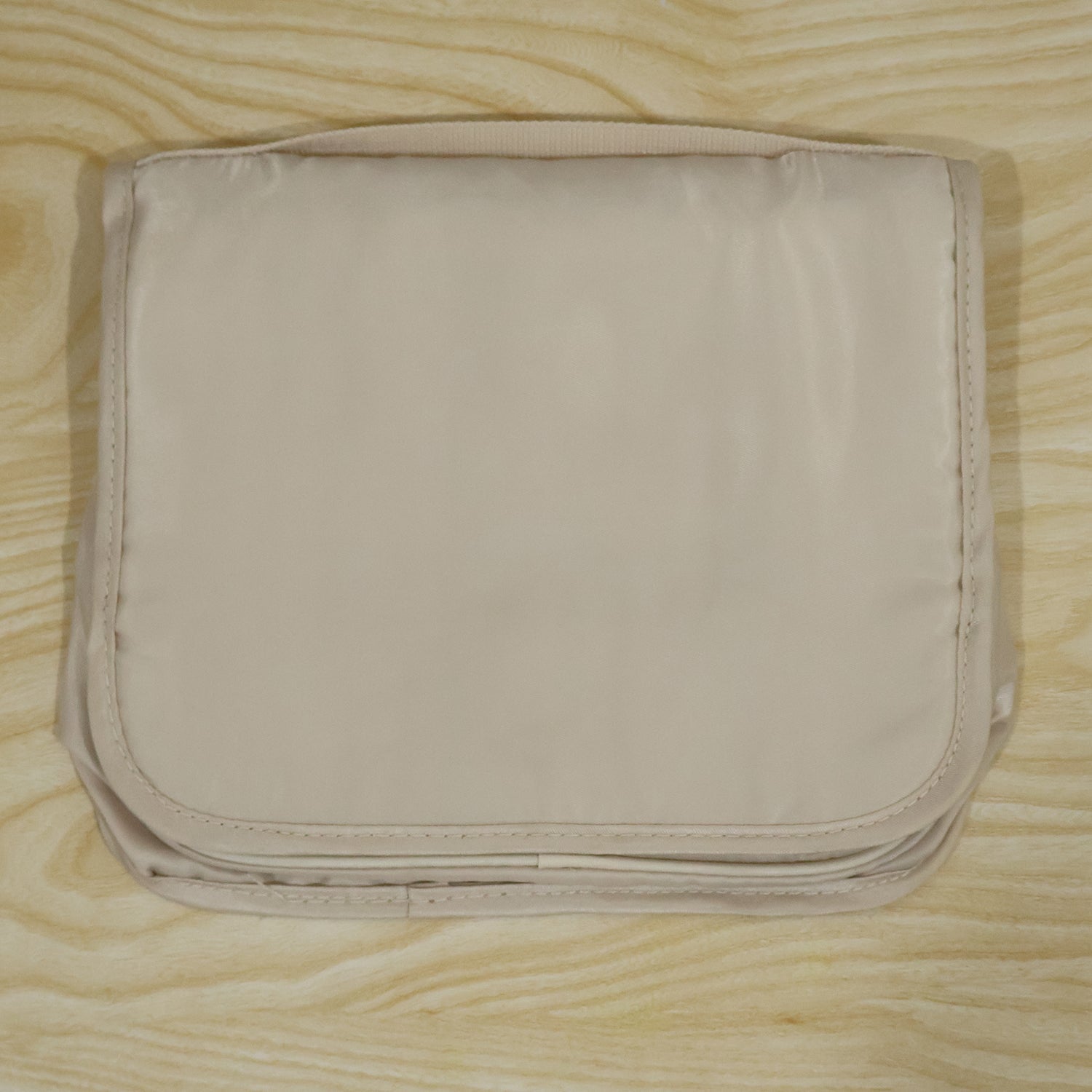 A neatly folded beige toiletry bag with a subtle sheen, resting on a light wooden background.
