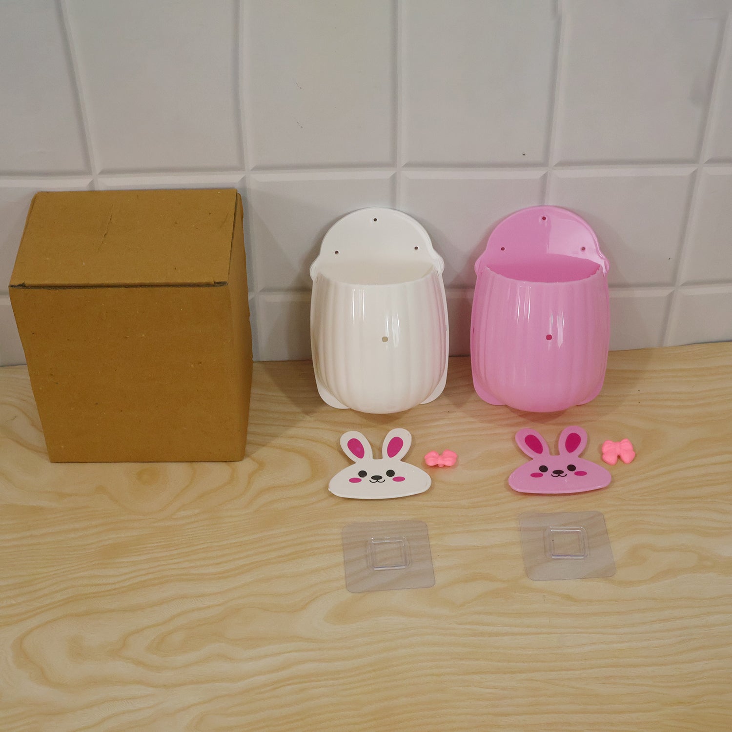 Disassembled white and pink organizers, hooks, and a brown cardboard box on a light wooden surface.