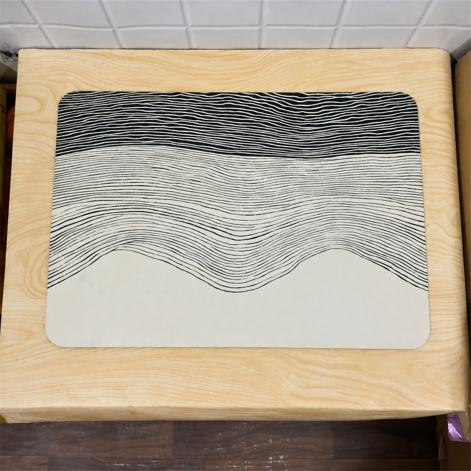 A rectangular mat with a black and white wavy line design rests on a light wooden surface.