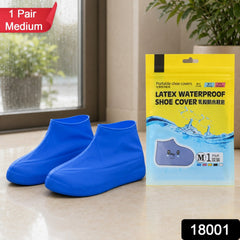 Two blue latex shoe covers and their packaging on a tiled floor, with a red "1 Pair Medium" label and black "18001" label.