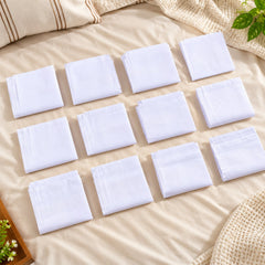 Twelve neatly folded white cotton handkerchiefs with subtle striped patterns are arranged on a light-colored bedspread.