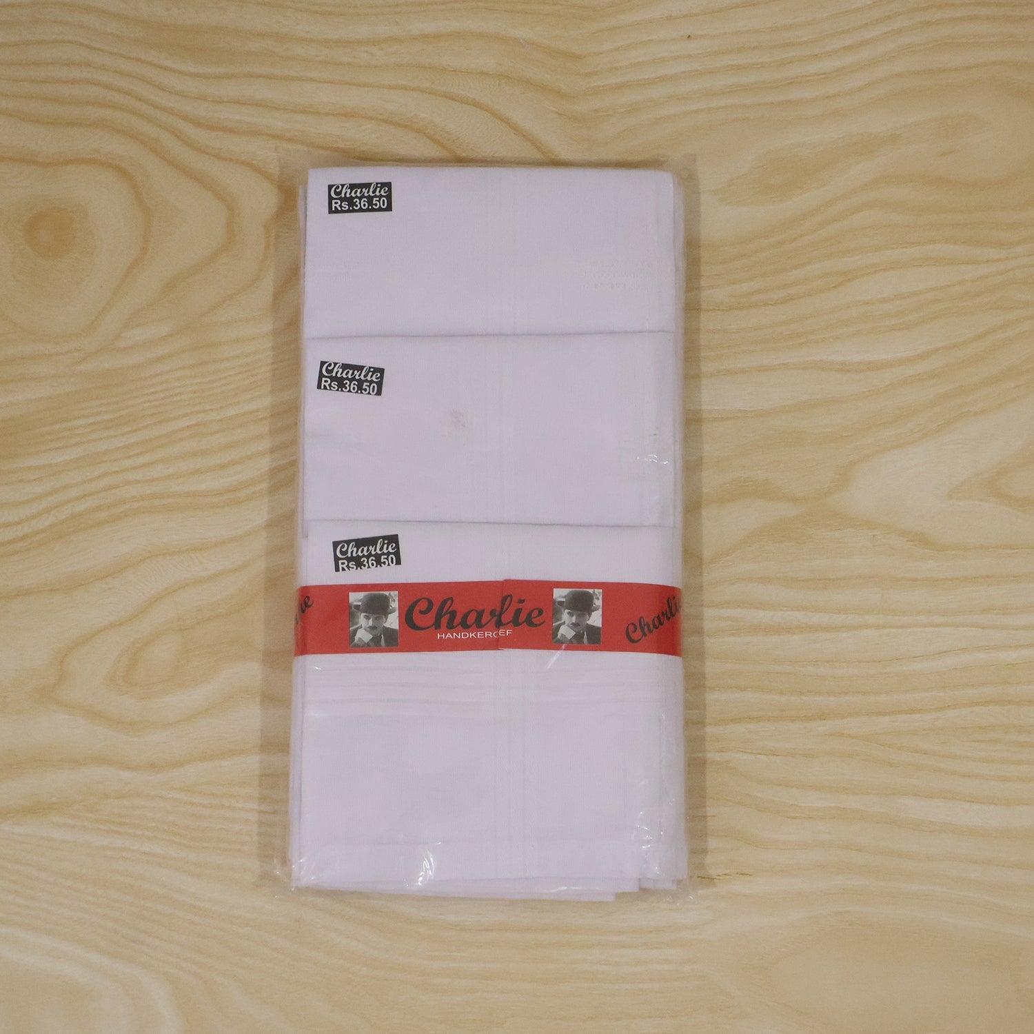 Multiple white handkerchiefs, branded "Charlie," are stacked and wrapped in clear plastic on a wooden surface.