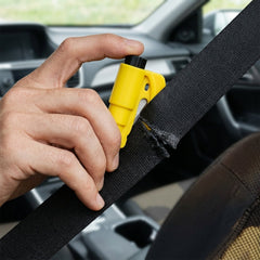 A hand uses a yellow car safety hammer to cut a black seat belt, which is partially frayed from the action, inside a car.