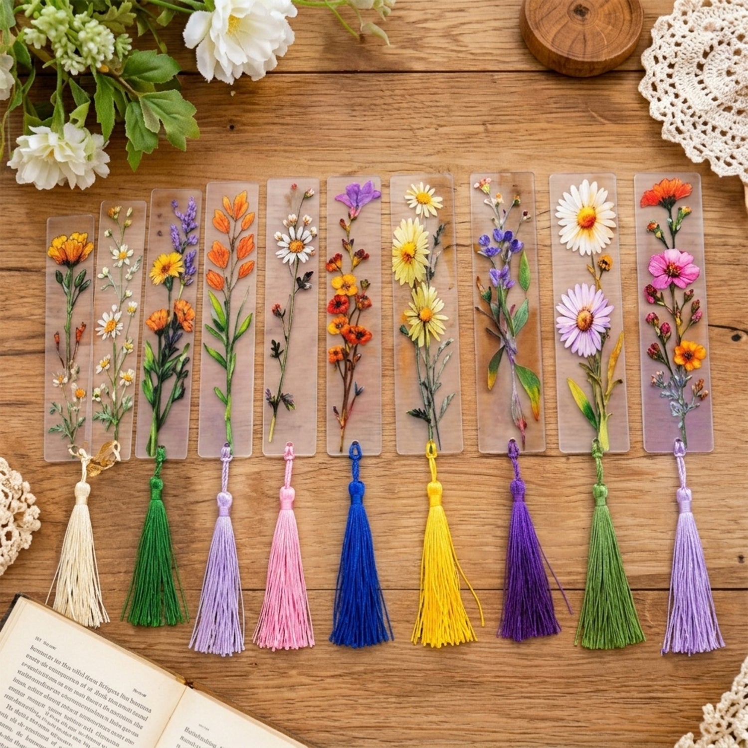 Ten transparent bookmarks with unique floral designs and colorful tassels are laid out on a wooden table.